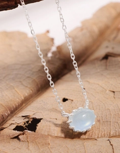 Macro shot of oval aquamarine gemstone pendant on S925 silver chain over dried leaf