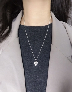 Detailed view of an S925 silver heart necklace with floral engraving worn by a model