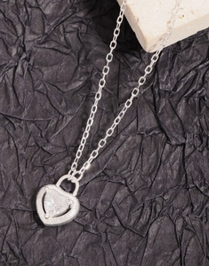 Detail shot of a sterling silver heart pendant with clear zircon on a dark textured background