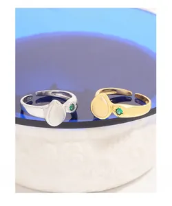 Close-up of pear-shaped cream stone rings with green zircon on textured ceramic