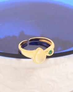 Close-up of adjustable gold ring with pear-shaped white stone and green accent gem