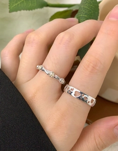 Detail showing stacked silver rings with hollow heart patterns and tiny pearl accents