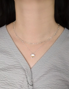 Close-up of double-layered silver necklace featuring a heart-shaped opal pendant on a model