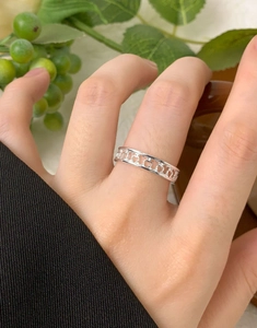 Detail of S925 sterling silver hollow heart ring worn on finger with natural green background