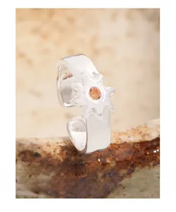 Macro shot of silver sunburst ring with orange gemstone on rustic ceramic base
