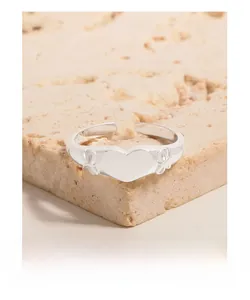 Close-up of S925 sterling silver heart ring with bow accents on a textured stone base
