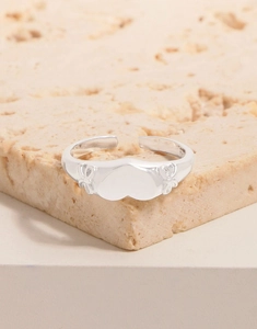 Macro shot of S925 sterling silver bow and heart ring on a beige stone surface