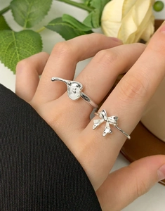 Close-up of S925 silver irregular heart and bow rings worn on a hand with floral accents
