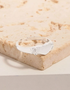 Macro shot of silver heart ring with bow relief details on a textured stone base