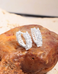 Detail of silver huggie earrings with cubic zirconia stones on natural stone base