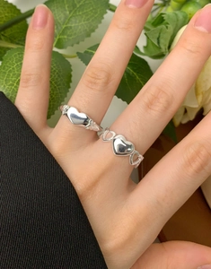 Close-up of two S925 sterling silver bow heart rings worn on a model hand with plants