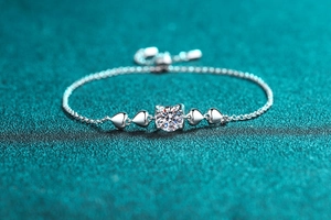 Macro shot of silver Moissanite bracelet with heart charms on green texture