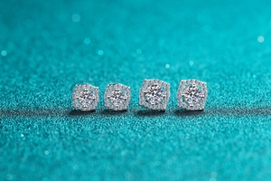 Macro shot of four silver square halo moissanite stud earrings on a teal glitter surface