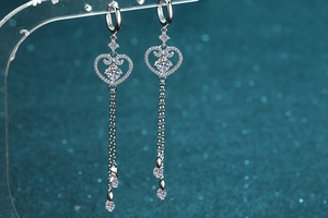 Macro shot of silver S925 heart tassel earrings with moissanite on a teal bokeh background