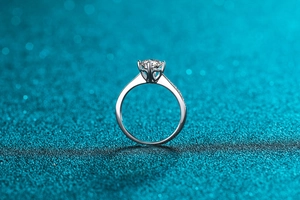 Macro side view of a six-prong silver moissanite ring with heart cutouts on blue glitter
