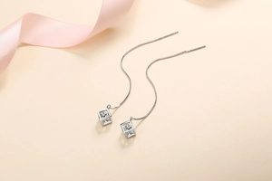 Macro shot of silver cube tassel earrings with sparkling zircon on silk background