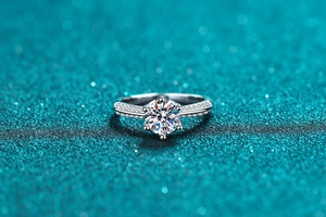 Macro shot of six-prong moissanite ring with micro-paved band on teal glitter background