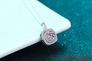 Macro shot of silver halo pendant with pink gems and white stones on a green background
