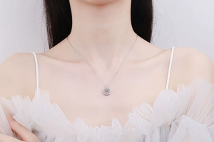 Close-up of a square 925 silver pendant necklace with pink accents on a white lace dress