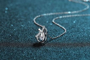 Close-up of S925 sterling silver bow pendant with round moissanite on a blue bokeh background