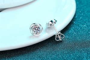 Macro shot of silver whirlwind earrings with moissanite set in a white ceramic dish