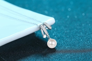 Macro detail of S925 silver crossover pendant with sparkling zircons and a white pearl