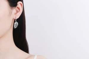 Detail of silver leaf-shaped drop earring with fine veins on model's ear