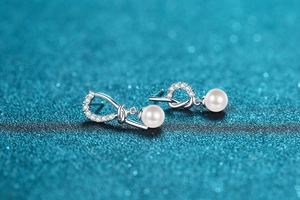 Macro detail of asymmetric S925 silver knot earrings with pavé crystals and freshwater pearl