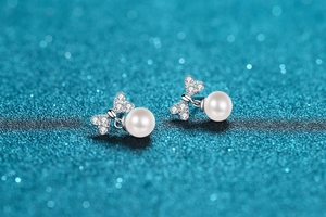 Macro shot of silver bow pearl earrings with cubic zirconia on a blue glitter background
