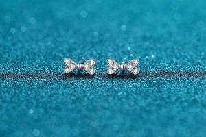 Detail of silver bow earrings with micro-pave zircon on dark blue glitter background