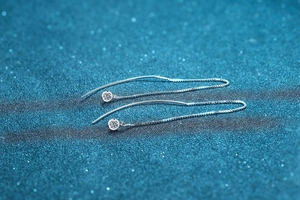Detail of S925 sterling silver threader earrings with round moissanite drop on blue background