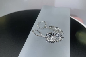 Detail of silver leaf hoop earrings with polished texture and intricate vein patterns