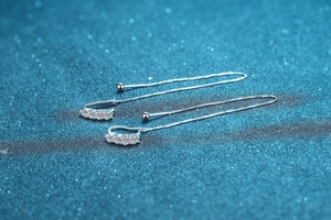 Macro view of S925 sterling silver ear wires with U-shaped Moissanite stones on blue glitter