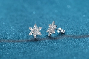 Macro detail of silver snowflake stud earrings with sparkling crystals on blue background