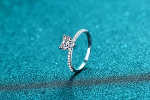 Close-up of heart-cut moissanite ring with side accent diamonds on blue glitter