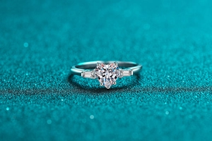 Macro d'une bague moissanite en forme de cœur avec pierres baguette sur fond sarcelle