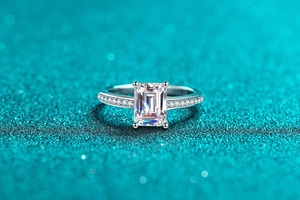 Macro shot of emerald cut moissanite ring with side diamonds on green glitter