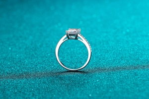Close-up of emerald cut moissanite ring with diamond accents on a blue glitter background