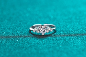 Macro shot of heart-cut moissanite ring with side accent diamonds on blue glitter