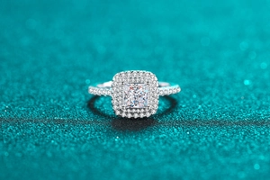 Vue macro d'une bague halo en moissanite taille princesse sur fond bleu scintillant