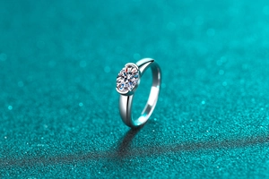 Macro shot of silver moissanite solitaire ring with polished metal on teal background