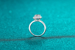 Détail d'une bague moissanite taille princesse avec halo sur fond texturé vert sarcelle