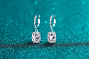 Macro shot of silver emerald-cut halo earrings on a sparkling blue bokeh background