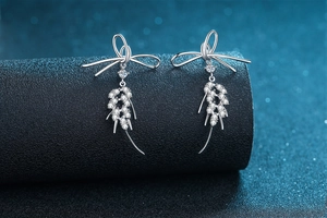 Detail of 925 sterling silver bow earrings with moissanite fringe on a dark blue stand