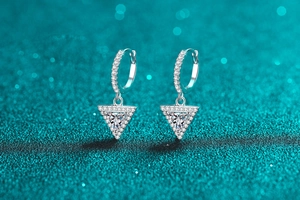 Macro shot of silver triangle drop earrings with sparkling pavé stones on a blue glitter surface