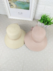 Detail of woven straw sun hats with ribbon bows in beige and pink on floral fabric