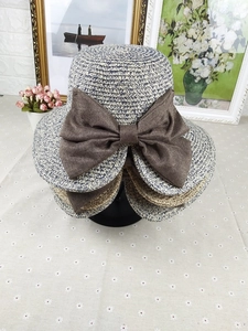 Close-up of woven straw sun hat with large dark brown bow on floral tabletop