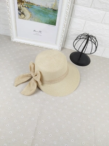 Close-up of a beige woven straw visor hat featuring a large decorative matching bow