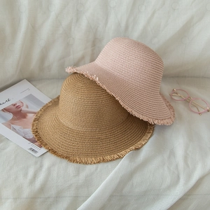 Detail of pink and khaki straw sun hats with trendy fringe edges on white fabric