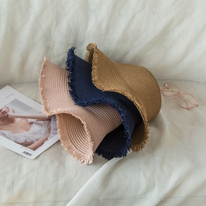 Three straw hats with fringed edges in beige, navy, and camel on a white cloth backdrop